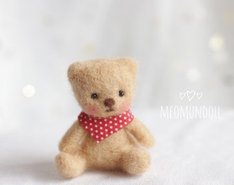 May include: A miniature, beige teddy bear wearing a red polka-dot scarf. The bear has a brown nose and pink cheeks. The doll is seated on a white surface. The text "MEOMUNDOLL" is visible in white.