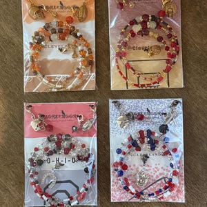 Puede incluir: Cuatro conjuntos de joyas hechos a mano con pulseras de cuentas y pendientes a juego. Cada conjunto incluye dijes temáticos deportivos como balones de fútbol, baloncesto y cascos. Los esquemas de color varían, incluyendo naranja, rojo, blanco y azul, con la marca "LORESMOOR".