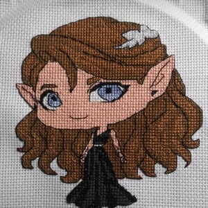 May include: Cross-stitch embroidery of a cartoon elf with long brown hair, wearing a black dress and a white flower in her hair.