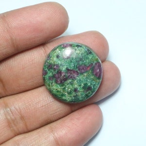 May include: A round green gemstone with red and gold flecks. The gemstone is cabochon cut and has a smooth, polished surface.