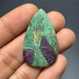 Op de afbeelding: Een peervormige cabochon edelsteen met een getextureerde groene matrix met opvallende dieppaarse insluitingen. De steen vertoont een natuurlijk, onregelmatig oppervlak met zichtbare minerale aders en kristallijne patronen over het hele oppervlak.