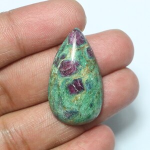 May include: A teardrop-shaped cabochon gemstone with a green base and red ruby inclusions. The stone is polished and has a smooth surface.