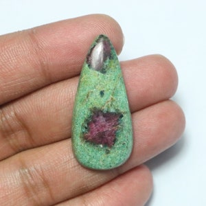 May include: A teardrop-shaped cabochon gemstone with a green base and pink and red inclusions. The stone is approximately 2.5 cm long.
