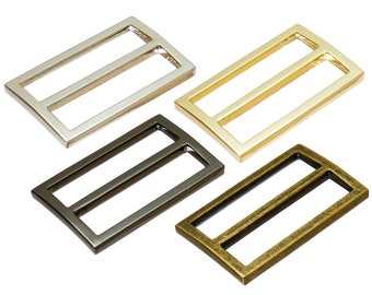 May include: Four metal slider buckles in different finishes: silver, gold, black, and antique brass. Each buckle has a rectangular shape with rounded corners and two parallel slots.
