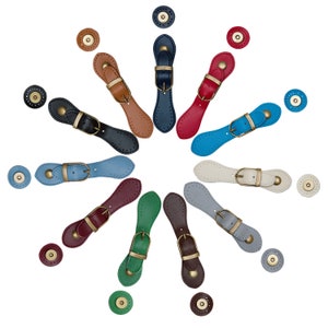 May include: Assortment of 12 leather button closures in various colours, including red, blue, green, brown, and white. Each closure features a metal buckle and a matching snap button.