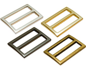 May include: Four metal slider buckles in different finishes: silver, gold, black, and antique brass. Each buckle has a rectangular shape with a rounded edge and a single, centered, horizontal slot.