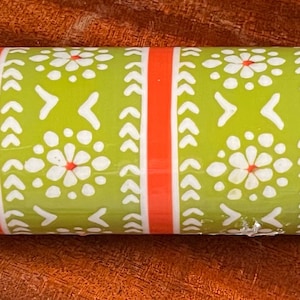 May include: A rolling pin with wooden handles and a patterned center. The center features a green background with white floral and geometric designs, accented by red vertical stripes. The handles are made of light-colored wood.
