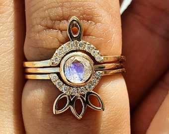May include: A gold ring featuring a moonstone centre stone encircled by a halo of small diamonds. The ring has a delicate, floral design with five petals.