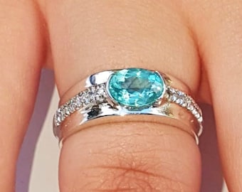 May include: A silver ring with a light blue oval gemstone surrounded by smaller clear gemstones.