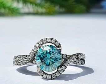 Könnte beinhalten: Ein silberner Ring mit einem großen, runden, blaugrünen Edelstein, der von einem Heiligenschein aus kleineren Diamanten umgeben ist. Der Ringarm ist verdreht und mit kleineren Diamanten besetzt.