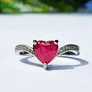 May include: A silver ring with a heart-shaped ruby gemstone and small diamonds on the band.