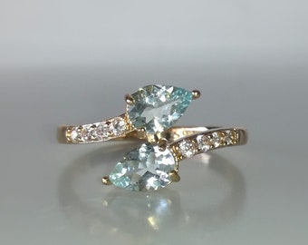 May include: A gold ring with two pear-shaped aquamarine gemstones and a band of small diamonds.