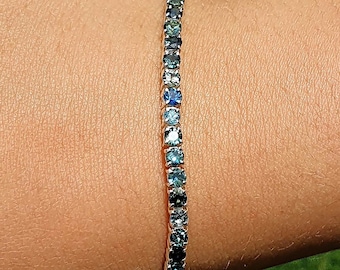 May include: A silver tennis bracelet with a row of blue gemstones.