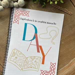 May include: A white spiral bound journal with the text "Supplications to be completed during the day" and the word "DAY" in large colorful letters. The journal has a red, orange, and gold geometric design on the cover.