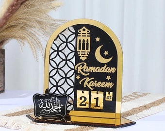 May include: A gold and black Ramadan calendar with a crescent moon, star, and lantern design. The calendar features the words "Ramadan Kareem" and the number "21st".