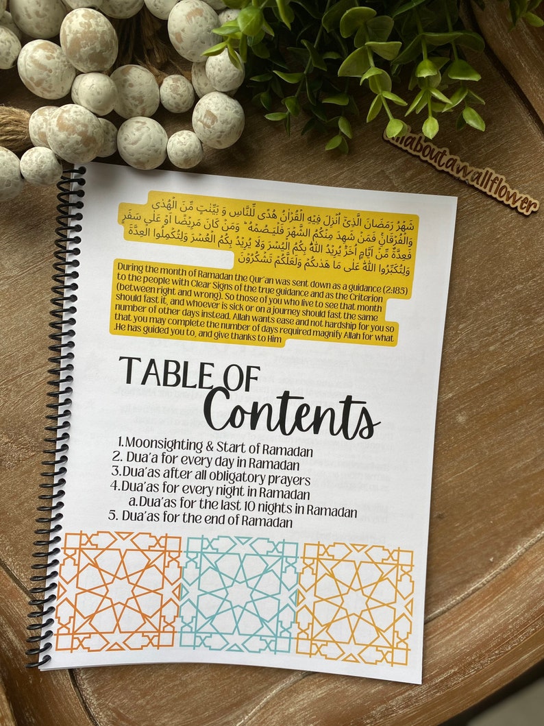 May include: A white and yellow spiral bound notebook with a table of contents for Ramadan prayers. The notebook has a gold background with Arabic text and a gold border.