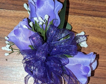 May include: A purple silk rose boutonniere with a sparkly purple bow and white baby's breath.