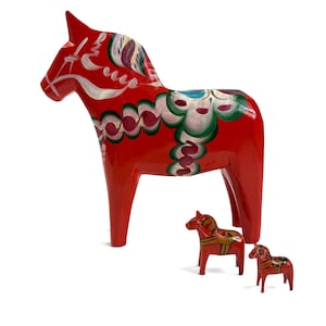 May include: A large red wooden horse figurine featuring intricate white, green, and blue painted floral patterns, accompanied by two smaller red wooden horse figurines with similar painted details on their bodies and saddles.