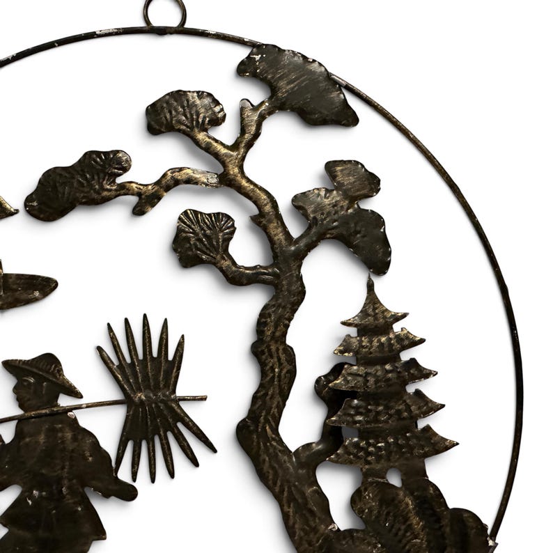 May include: A circular wall hanging made of dark, textured metal featuring a silhouette design. The artwork depicts a person wearing a conical hat carrying a bundle on a pole, a tall tree with textured foliage, and a multi-tiered pagoda structure.
