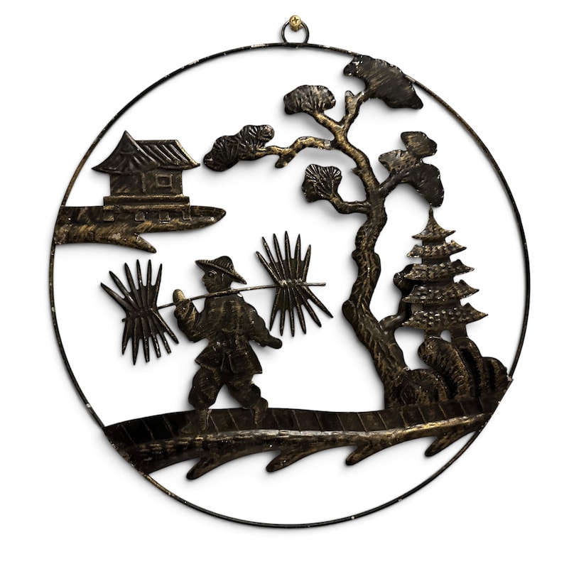 May include: A circular black and gold metal wall art piece featuring a silhouette of a person carrying a pole with bundles across their shoulders, a small house, a pagoda, and a tree, all enclosed within a thin metal ring frame.