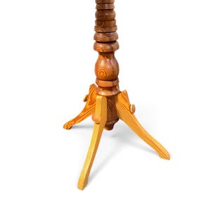May include: A wooden stand featuring a tall, vertically stacked, turned-wood central column with a prominent grain pattern. The base consists of three angled, light-coloured wooden legs attached to the central post with circular fasteners.