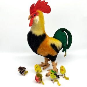May include: A large stuffed rooster with a red comb, yellow neck, black chest, and orange and yellow body. Several small stuffed chicks in various colors are at the rooster's feet. The rooster has brown legs and a green tail.