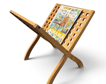 May include: A light brown wooden magazine rack with a lattice design and curved legs. A magazine titled RETRO with the text KOKA BLA on the cover is resting on the rack. The structure is made of interconnected wooden slats forming a display stand.