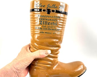 May include: A tan ceramic boot-shaped mug featuring a black strap detail at the top. The text reads Salve Julho 1968, 13º aniversário, RESTAURANTE ZILLERTAL, Tel, 37-6772, Av. Brig. Luiz Antonio, 909, SÃO PAULO SP in black lettering on the front.