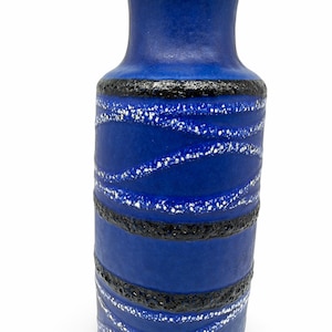 May include: A cylindrical ceramic vase featuring a vibrant blue matte finish. The surface is decorated with horizontal bands of textured black lava glaze and wavy, diagonal lines of white speckled glaze that wrap around the body.