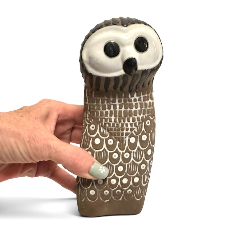 K&ouml;nnte beinhalten: Eine Eulenfigur aus Keramik mit wei&szlig;em Gesicht, gro&szlig;en schwarzen Augen und einem schwarzen Schnabel. Der K&ouml;rper ist braun mit einem wei&szlig;en Gittermuster auf der Brust und einem wei&szlig;en Schuppenmuster im unteren Bereich, akzentuiert durch kleine wei&szlig;e Kreise.