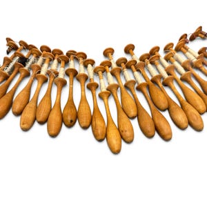 May include: A collection of numerous light brown wooden bobbins arranged in a curved formation. Each bobbin features a slender handle and a wider top section, with several wrapped in thin white thread and one wrapped in black thread.
