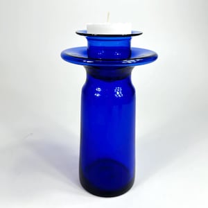 Op de afbeelding: Een kobaltblauwe glazen kaarsenhouder met een brede, platte bovenkant en een kleinere, ronde bovenkant om een kaars te houden. De kaarsenhouder is gemaakt van dik glas en heeft een gladde, gepolijste afwerking.