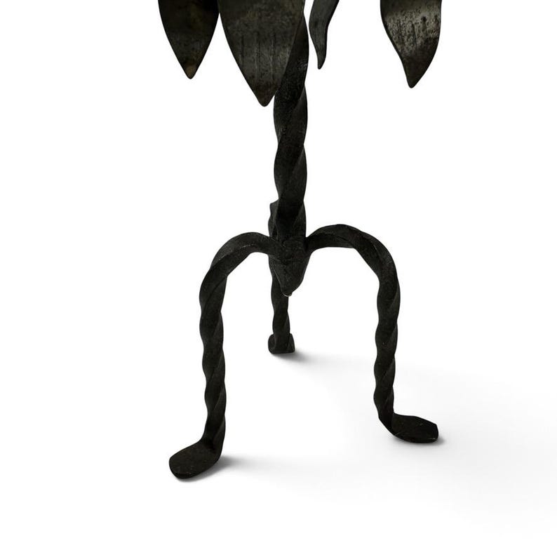 May include: A black wrought iron candle holder featuring a central twisted stem supported by three curved, twisted legs. The top section displays several pointed, leaf-shaped metal elements arranged in a circular pattern around the center.