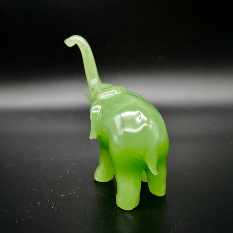 K&ouml;nnte beinhalten: Eine durchscheinende, hellgr&uuml;ne Elefantenfigur mit erhobenem R&uuml;ssel. Die Figur hat eine glatte, gl&auml;nzende Oberfl&auml;che und ist vor einem dunklen Hintergrund platziert. Der Elefant ist ein dekorativer Gegenstand.