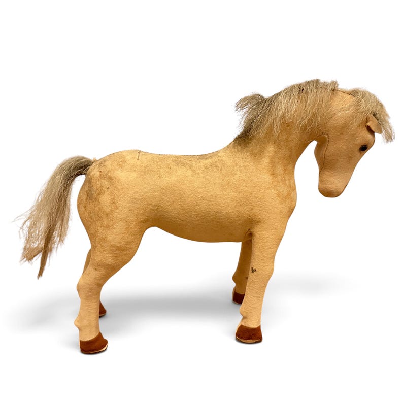 May include: A tan-colored horse figurine with a textured surface, featuring a long, light-colored mane and tail made of synthetic fibers. The horse stands in a downward-facing position with dark brown hooves and small, dark, circular eyes.