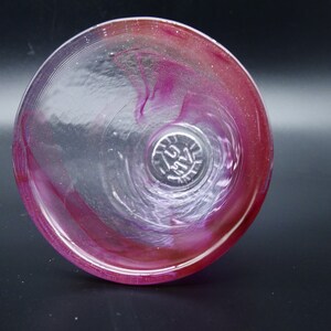 Puede incluir: Copa de vino de cristal transparente con un dise&ntilde;o en espiral de tonos rosas y rojos. La copa tiene un cuenco ancho y un dise&ntilde;o sin tallo. La parte inferior de la copa tiene una marca circular. La copa est&aacute; sobre un fondo oscuro.