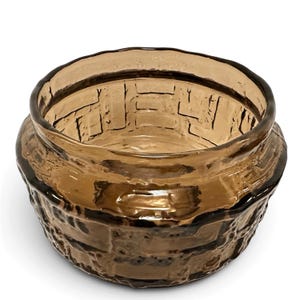 May include: A round, amber-colored glass bowl featuring a textured, raised brick-like pattern on its exterior surface. The glass is translucent with a smooth, thick rim and a wide, open top, showcasing a consistent brown hue throughout the piece.