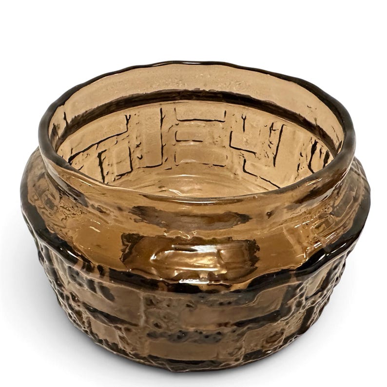 May include: A round, amber-colored glass bowl featuring a textured, raised brick-like pattern on its exterior surface. The glass is translucent with a smooth, thick rim and a wide, open top, showcasing a consistent brown hue throughout the piece.