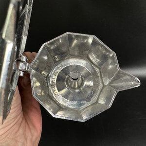 Puede incluir: Cafetera de metal plateado con una parte superior redonda abierta y un pico. La cafetera tiene una etiqueta que dice "Made in Italy".