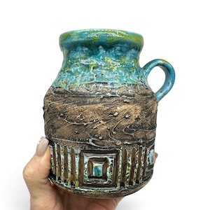 May include: A ceramic mug featuring a textured, dark brown base with vertical grooved patterns and a square relief design. The upper section is finished in a glossy, vibrant turquoise and lime green glaze, complemented by a matching curved handle.