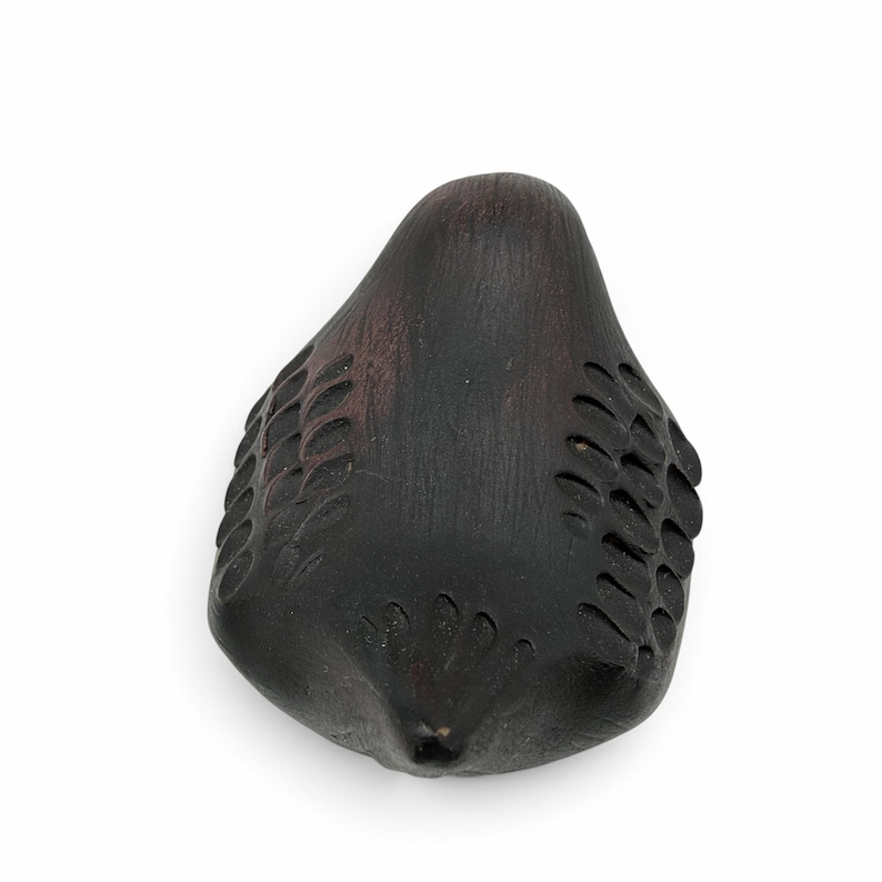May include: A dark brown, carved wooden bird figurine with a smooth, rounded body and stylized, incised feather patterns along the wings and tail. The surface shows a deep, matte finish with subtle wood grain texture throughout the piece.