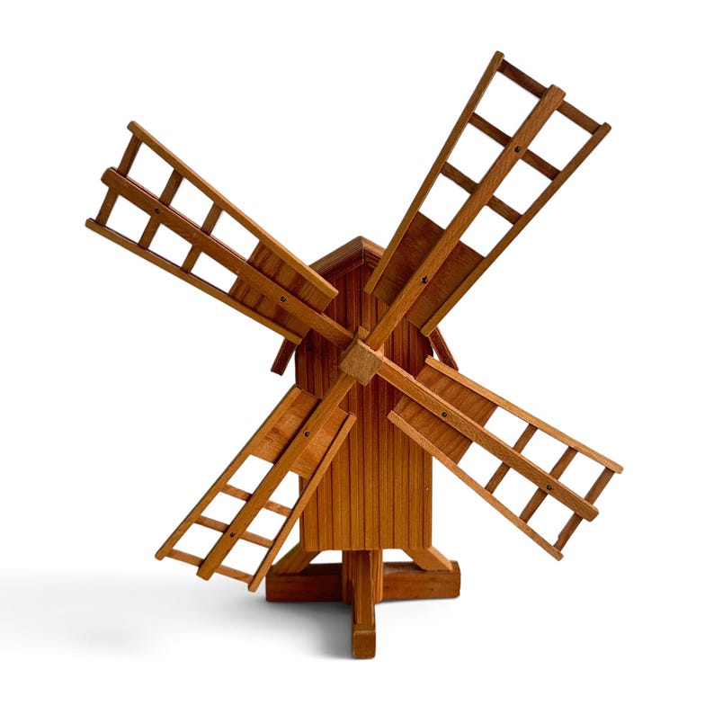 May include: A wooden windmill model featuring a central tower with vertical slats and four large, grid-patterned blades attached to a central hub. The structure is crafted from light brown wood and stands on a sturdy, multi-legged base support.