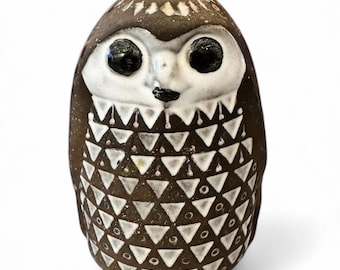 May include: A ceramic owl figurine with a brown and white geometric pattern. The owl has black eyes and a white beak.
