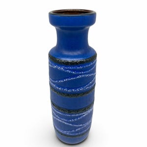 May include: A cylindrical ceramic vase with a vibrant blue matte finish. The body features horizontal bands of textured black glaze and diagonal white speckled patterns. The vase has a flared rim and a dark brown interior visible at the opening.