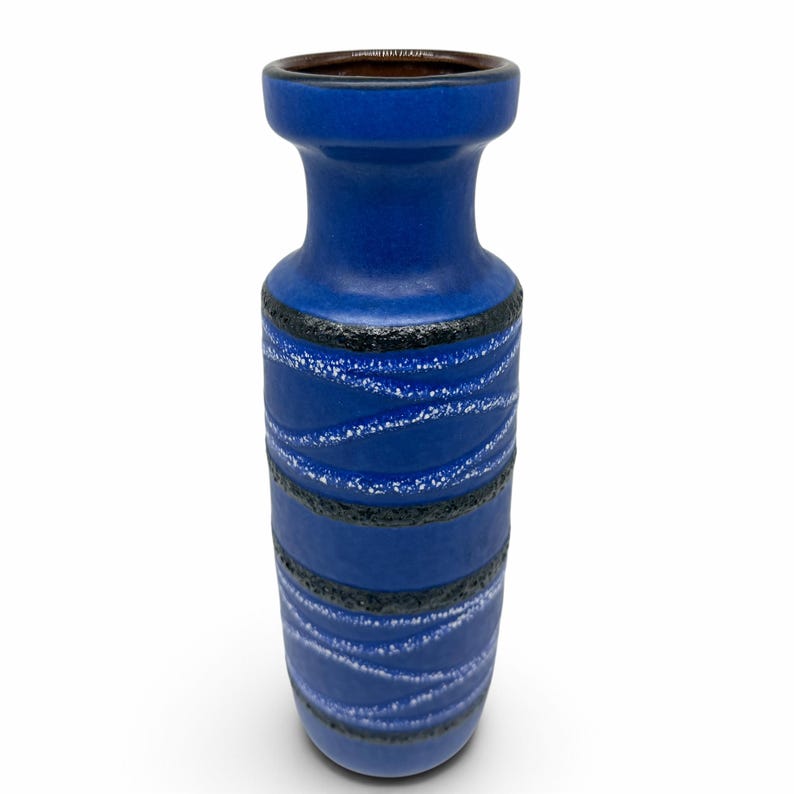 May include: A cylindrical ceramic vase with a vibrant blue matte finish. The body features horizontal bands of textured black glaze and diagonal white speckled patterns. The vase has a flared rim and a dark brown interior visible at the opening.