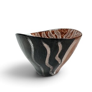 May include: A glass bowl with an asymmetrical rim, featuring a black exterior with vertical silver brushstroke patterns. The interior displays a textured brown finish with white wavy lines. The word "MOSER" is etched near the base of the bowl.
