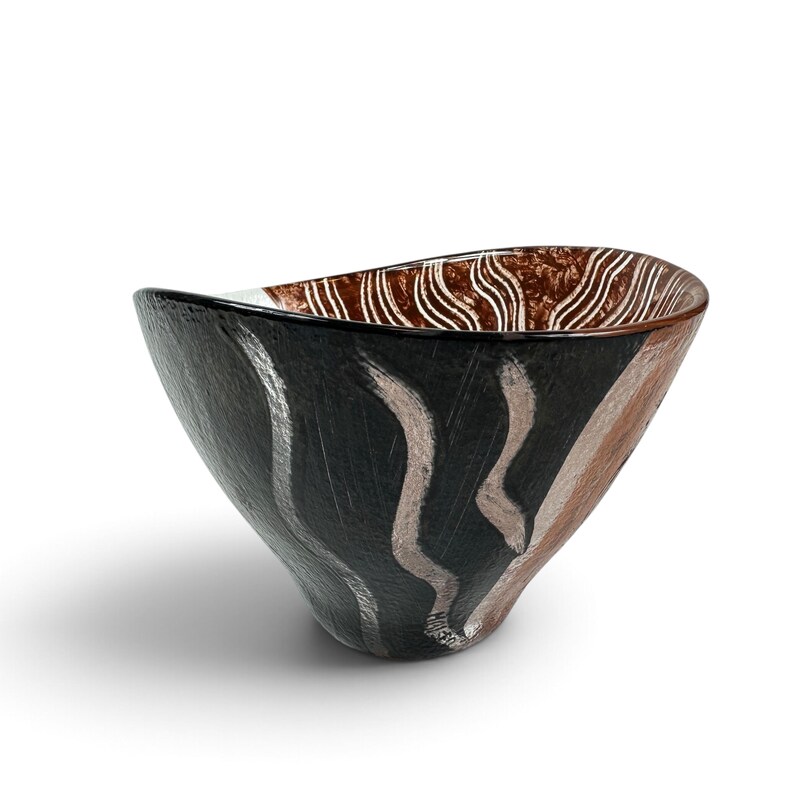 May include: A glass bowl with an asymmetrical rim, featuring a black exterior with vertical silver brushstroke patterns. The interior displays a textured brown finish with white wavy lines. The word "MOSER" is etched near the base of the bowl.