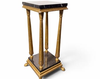 Peut inclure: Un piédestal carré doté d'un plateau et d'une base en marbre noir avec des accents en métal doré. La structure est soutenue par quatre colonnes fines et texturées, reposant sur quatre pieds ornés en forme de griffes.