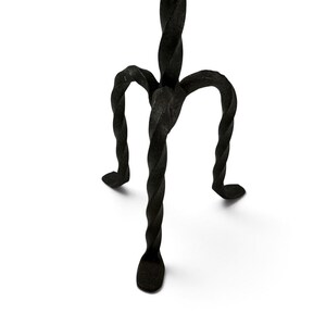 May include: A black metal stand featuring three legs with a distinct twisted, spiral design. The legs converge at a central point, supporting a vertical structure that extends upward. The metal has a textured, matte finish throughout the piece.