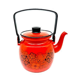 Puede incluir: Una tetera roja de esmalte con asa, tapa y diseño floral negros. La tetera tiene un cuerpo redondeado y un pico curvo. El diseño floral es negro y naranja. La tetera es de estilo vintage.